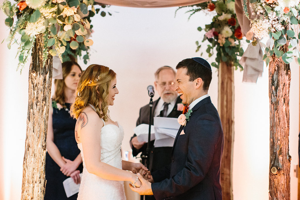 Bride and Groom laughing. Bride and Groom under wedding chuppah. Floral wedding arch. Moxie Bright Events.